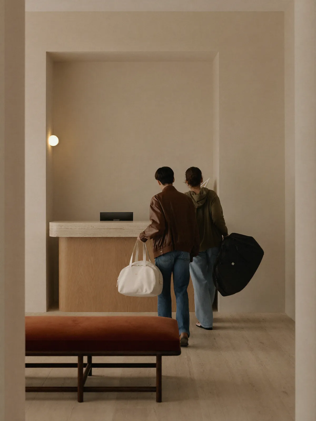 Zwei junge Reisende mit Wochenendtaschen beim Check-in in einer warmen, minimalistischen Hotellobby